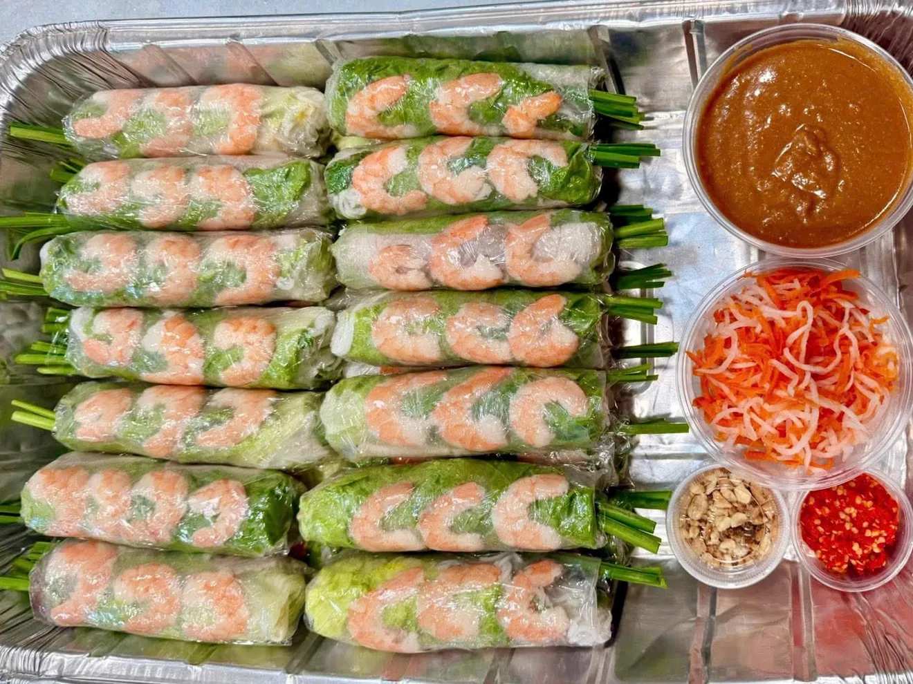 Shrimp spring rolls with leafy greens, dipping sauce, and pickled vegetables