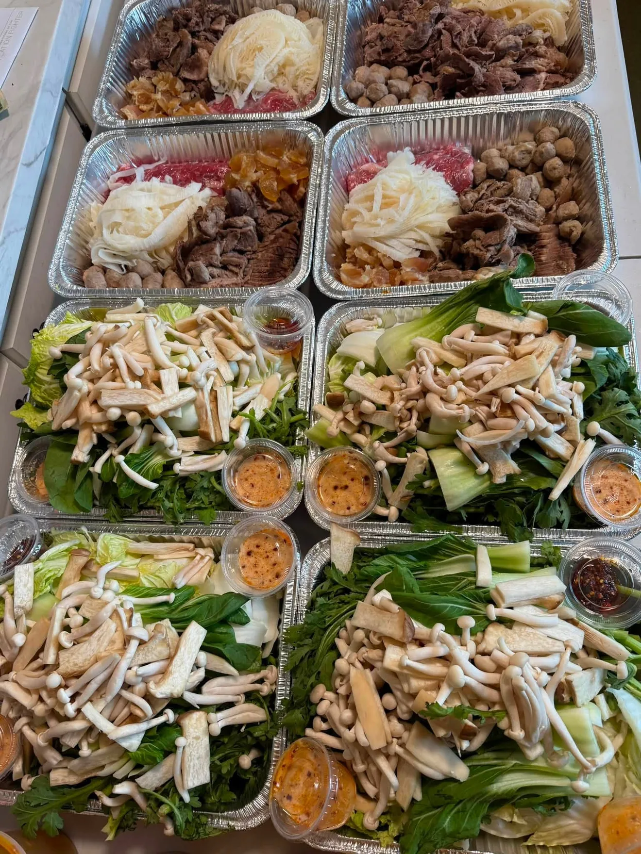 Takeaway trays of sliced meat, leafy greens, and mushrooms